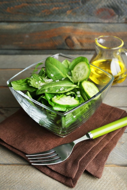 Ciotola di vetro di insalata verde con cetriolo e spinaci su sfondo di legno