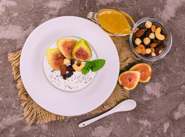 Ciotola di yogurt con noci di fichi e miele su uno sfondo grigio Spazio piatto per la copia