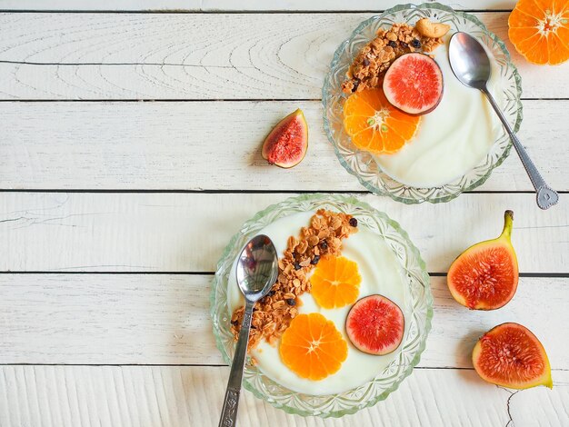 Ciotola di yogurt muesli condita con arancia fresca e frutta di fico su un tavolo di legno bianco