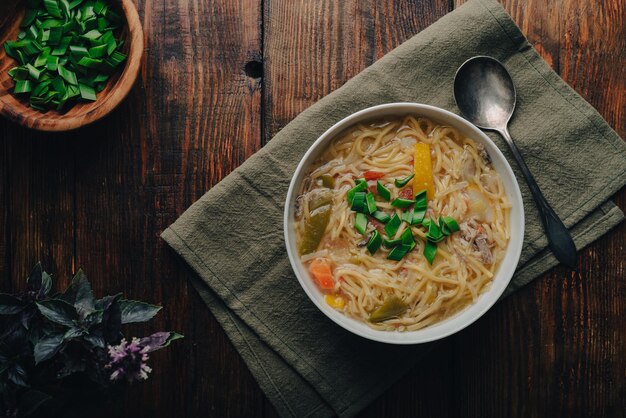 Ciotola di zuppa di noodle con verdure e carne di anatra su tavolo di legno vista dall'alto