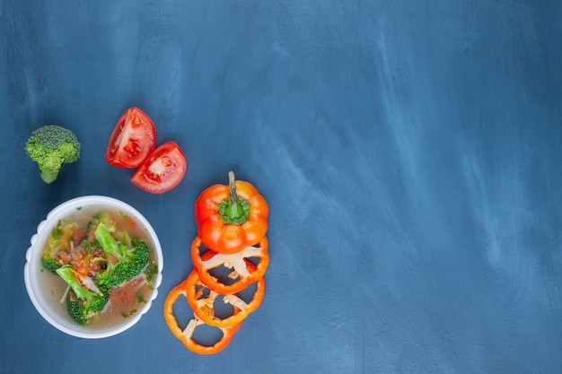 Ciotola di zuppa di pollo, verdure e pane, su sfondo blu.