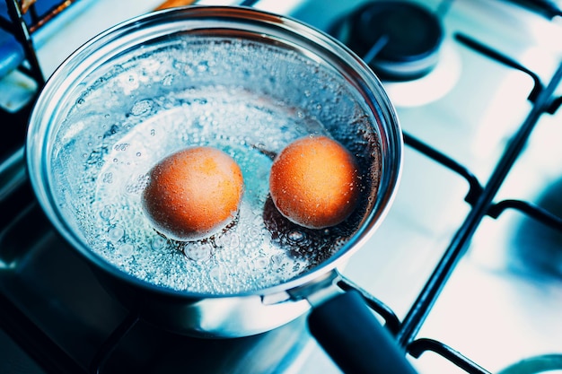 Ciotola in acciaio inossidabile con uova bollenti colazione in acqua su una stufa a gas