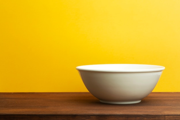 Ciotola in ceramica bianca su sfondo giallo. Piatto vuoto per insalata o zuppa sulla tavola di legno