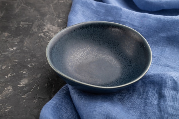Ciotola in ceramica blu vuota su sfondo di cemento nero e tessuto di lino blu