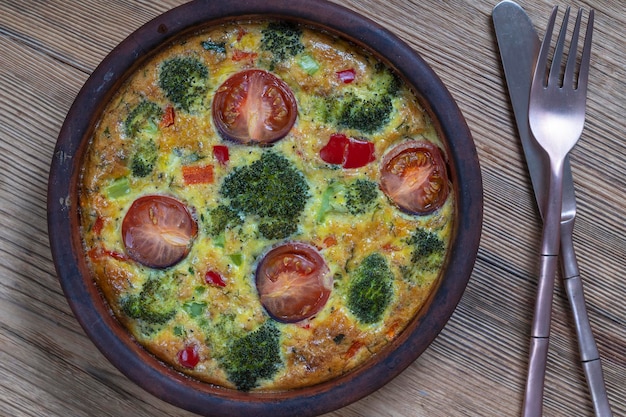 Ciotola in ceramica con frittata di verdure semplice cibo vegetariano Frittata con uovo pomodoro pepe cipolla broccoli e formaggio su tavola di legno Frittata di uova italiana