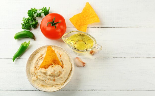 Ciotola in ceramica di gustosi hummus con patatine olio e verdure sul tavolo