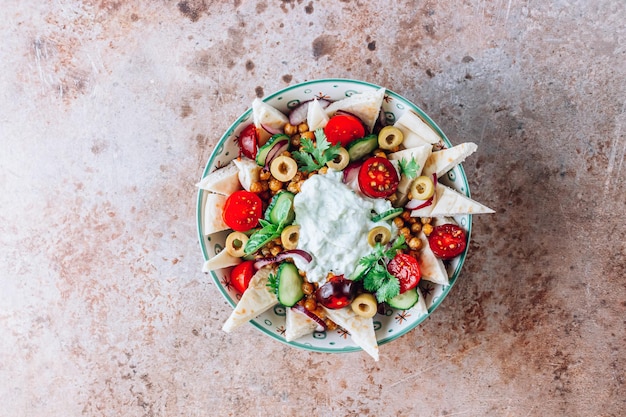 Ciotola mediterranea con ceci fritti, pita, olive, verdure fresche e salsa tzatziki su uno sfondo rustico beige