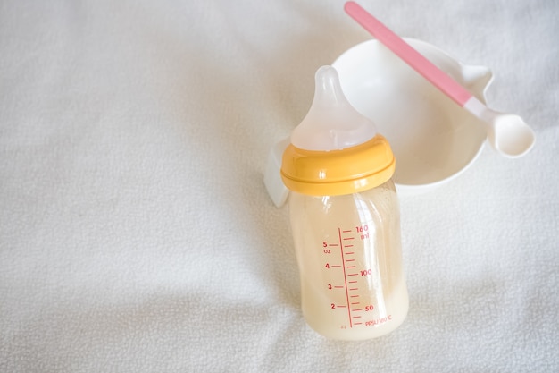 Ciotola per bimbi, cucchiaio e bottiglia di latte materno in bianco