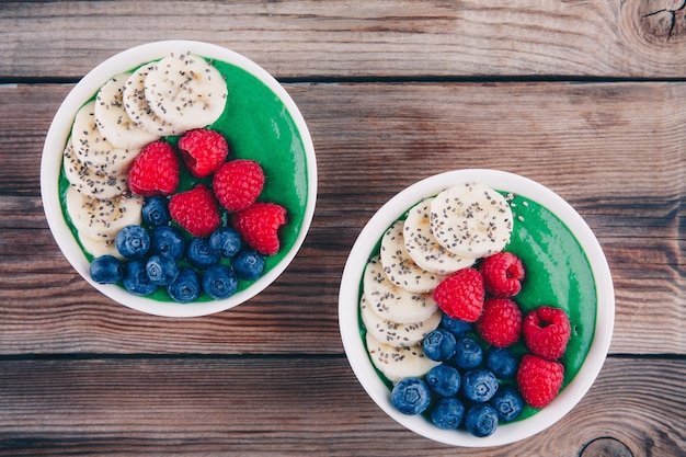 Ciotola per frullati sani per la colazione con polvere di spirulina, lamponi, banana, mirtilli, semi di chia e scaglie di cocco Vista dall'alto