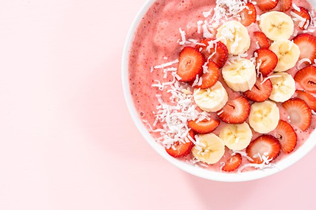 Ciotola per frullato di fragole e banana guarnita con scaglie di cocco e frutta fresca