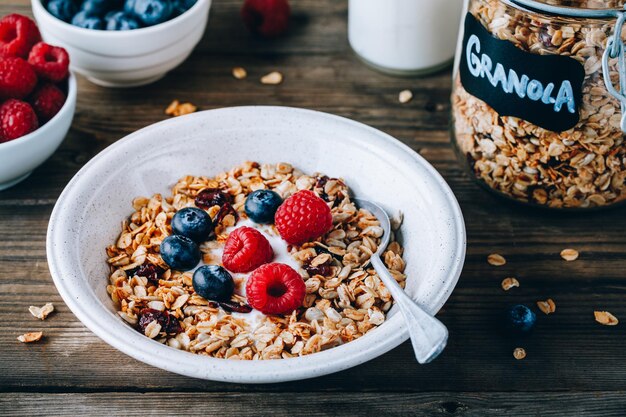 Ciotola sana per la colazione Granola fatta in casa con yogurt naturale, mirtilli e lamponi su uno sfondo rustico in legno