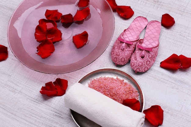 Ciotola Spa con acqua, petali di rosa, asciugamano e pantofole su sfondo chiaro. Concetto di pedicure o trattamento termale naturale