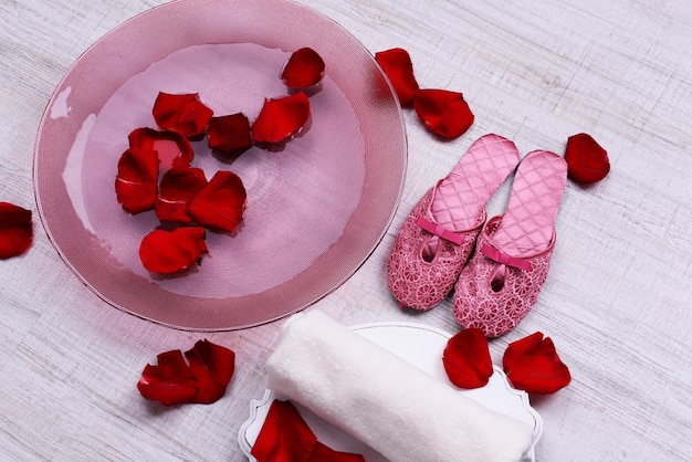 Ciotola Spa con acqua, petali di rosa, asciugamano e pantofole su sfondo chiaro. Concetto di pedicure o trattamento termale naturale