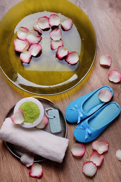 Ciotola termale con petali di rosa d'acqua asciugamano e pantofole su sfondo chiaro Concetto di pedicure o trattamento termale naturale