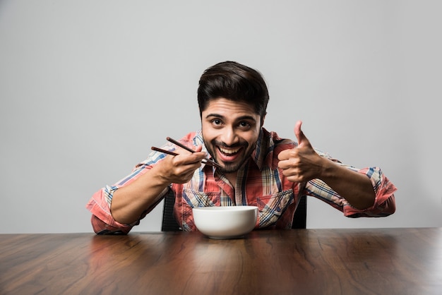 Ciotola vuota e uomo indiano con la barba che tiene cucchiaio o bacchette, indossa una camicia a scacchi e si siede al tavolo