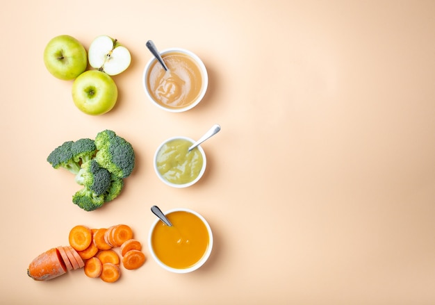 Ciotole bianche con alimenti per bambini naturali sani su sfondo pastello con spazio per il testo. Purea di frutta e verdura fresca, flay lay, vista dall'alto, concetto. Cibo per bambini a base di carote, broccoli, mele