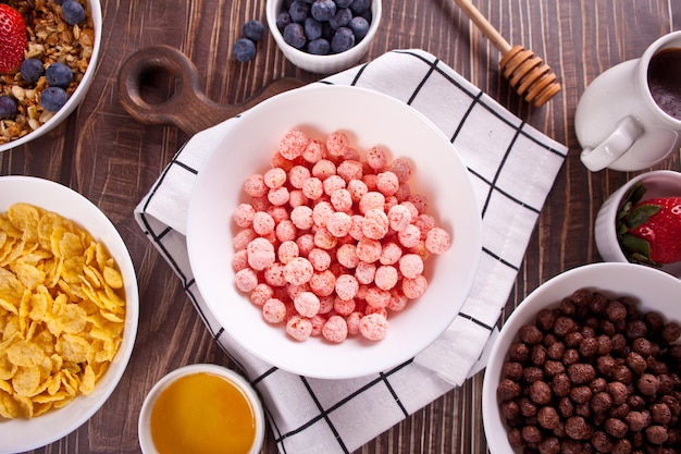 Ciotole con fragole, polpette di mais dolce al cioccolato, muesli e corn flakes con frutti di bosco. Cereali per la colazione deliziosi e salutari. Vista dall'alto.