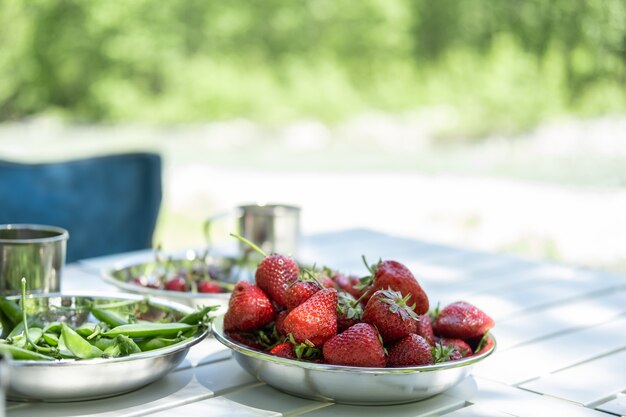Ciotole di fragole fresche di piselli verdi ciliegia sul tavolo da picnic in campeggio in estate