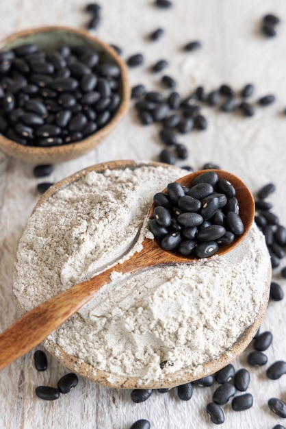 Ciotole in ceramica con farina di fagioli neri e fagioli secchi con un cucchiaio di legno in primo piano. Mangiare sano e concetto vegetariano. Ingrediente tradizionale cugino latinoamericano