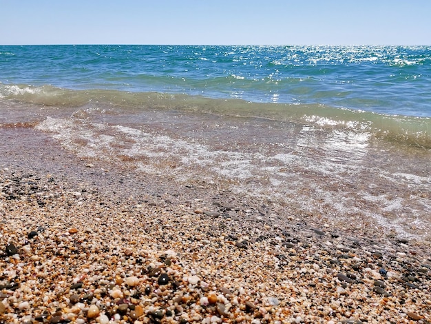 Ciottoli di mare onde del mare blu sole splendente La superficie blu brillante del mare Carta da parati del paesaggio