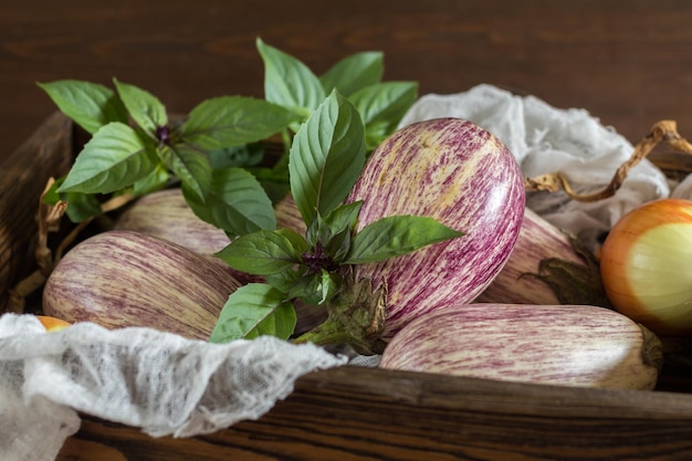 Cipolla di melanzane graffiti viola e basilico fresco verde in una scatola di legno in uno sfondo di legno d'epoca nel fuoco selettivo di stile rustico