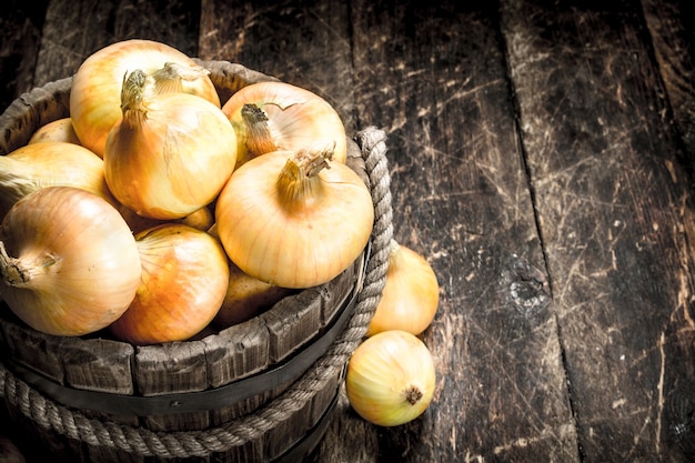 Cipolle fresche in un secchio di legno. Su uno sfondo di legno.