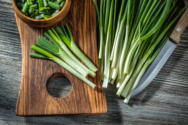 Cipolle tritate verdi sul fondo di legno dell'annata del coltello da cucina del tagliere di legno