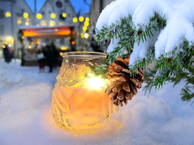città invernale, rami di albero di Natale con coni e fiocchi di neve accesi, lume di candela nella neve