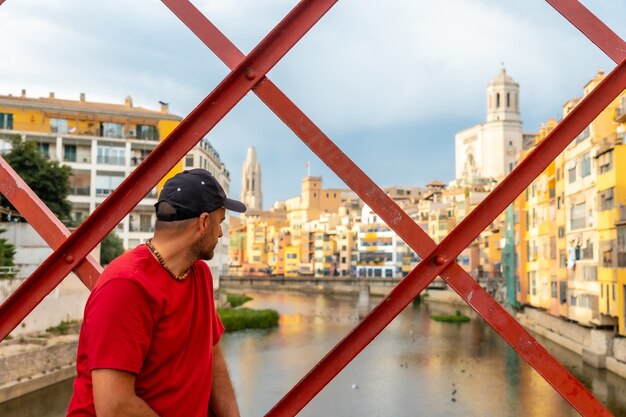 Città medievale di Girona, un giovane in rosso e con un berretto che guarda la città dal famoso ponte rosso Pont de les Peixateries Velles, Costa Brava della Catalogna