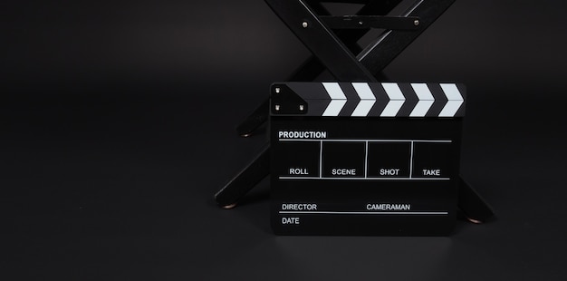 Clap board o ardesia cinematografica con sedia da regista utilizzata nella produzione video e nell'industria cinematografica su sfondo nero.