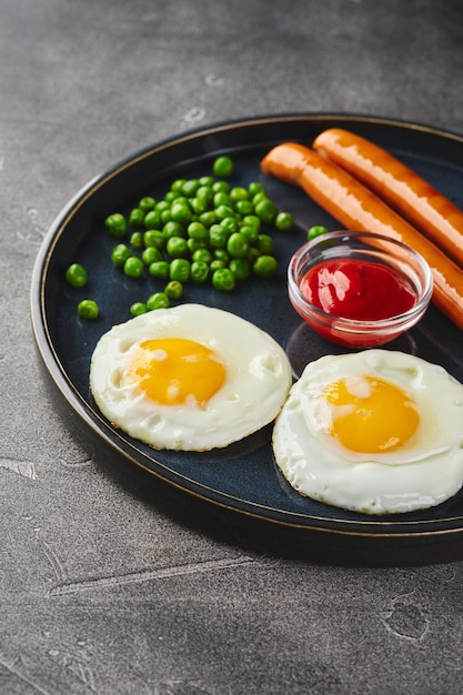 Classica colazione a base di uova fritte, salsicce e piselli sul piatto su sfondo grigio