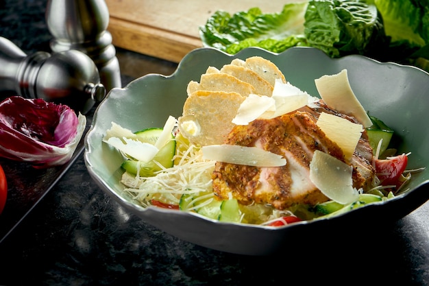 Classica insalata Caesar con crostini di pane, parmigiano, pollo alla griglia, servita in una ciotola verde su un tavolo di marmo scuro. Cibo del ristorante.