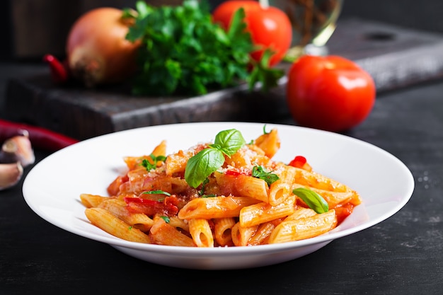 Classica pasta italiana penne alla arrabiata con basilico e parmigiano grattugiato fresco sul tavolo scuro. Penne al sugo di peperoncino all'arrabbiata.