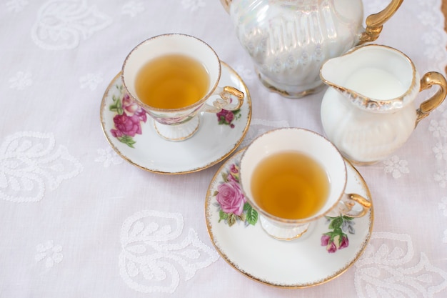 Classica tazza di tè bianco con rose sulla tovaglia bianca con barattolo di latte