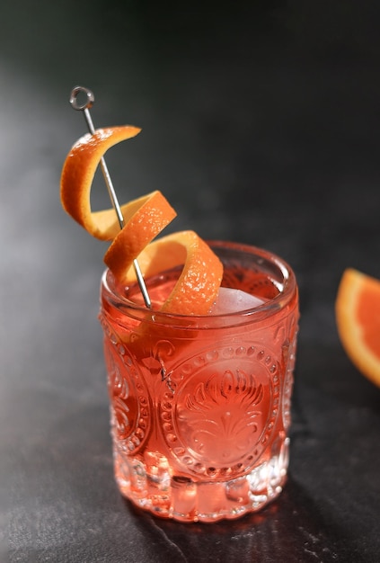 Classico cocktail Negroni in vetro retrò con ghiaccio e buccia d'arancia su sfondo nero