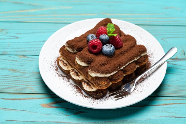 Classico dessert tiramisù con lamponi e mirtilli sulla tavola di legno blu