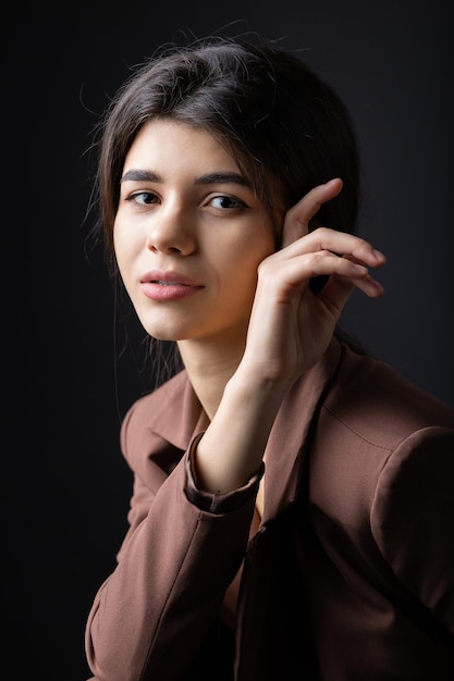 Classico ritratto in studio di una giovane bruna vestita con un top nero e un abito formale che è seduta su una sedia su uno sfondo nero