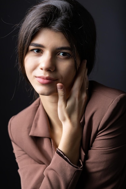 Classico ritratto in studio di una giovane bruna vestita con un top nero e un abito formale che è seduta su una sedia su uno sfondo nero