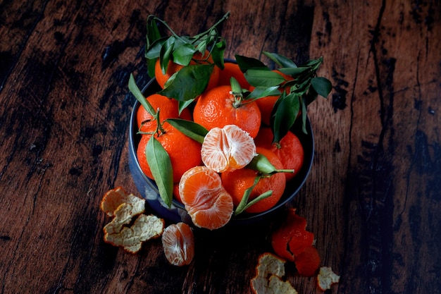 Clementine con foglie in un piatto di ceramica blu su un vecchio tavolo di legno