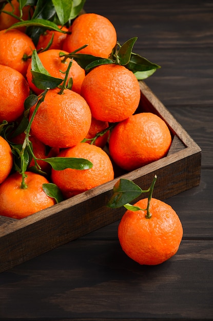 Clementine di mandarino fresco con foglie su fondo di legno scuro.