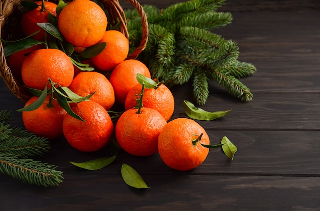 Clementine di mandarino fresco con foglie su fondo di legno scuro.