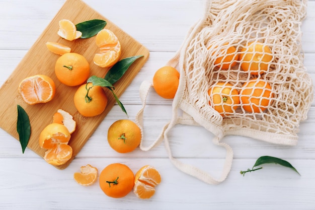 Clementine fresche con tagliere e borsa della spesa sul tavolo di legno bianco.