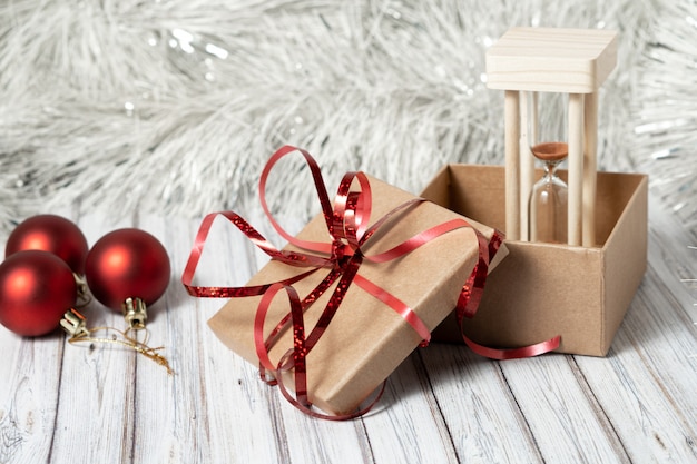 Clessidra e scatola di cartone su un tavolo di legno decorato con una ghirlanda e palle di Natale rosse per il nuovo anno o Natale. Concetto di posta, corriere o servizio di consegna. Copia spazio