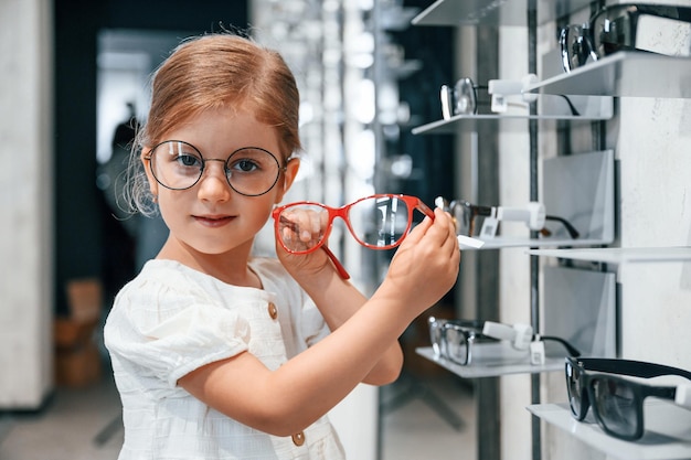 Cliente carino Bambina nel negozio di occhiali che sceglie gli occhiali