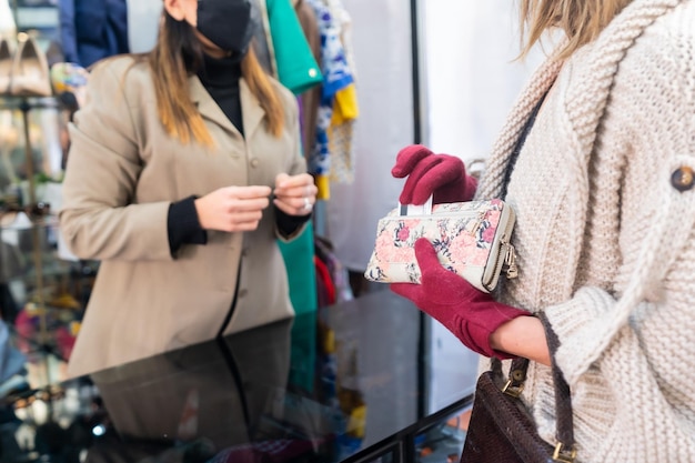 Cliente che paga con una maschera a un dipendente con maschere in un negozio di abbigliamento, misure di sicurezza nella pandemia di coronavirus, covid-19