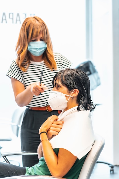 Cliente con maschera in un parrucchiere in pieno taglio di capelli. Misure di sicurezza per i parrucchieri nella pandemia di Covid-19. Nuova distanza normale, coronavirus, sociale