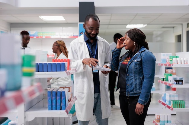 Cliente di farmacia che soffre di mal di testa, acquisto di antidolorifici, consulente di farmacia che raccomanda pillole per l'acquirente. Donna afroamericana che chiacchiera con il farmacista in farmacia, tutta la squadra nera