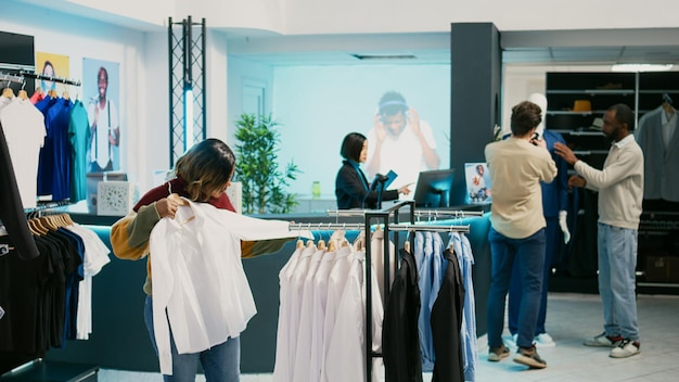 Cliente femminile che guarda la merce nel negozio di abbigliamento, acquista la nuova collezione alla moda. Giovane donna che controlla i vestiti appesi nei grandi magazzini, moderna boutique di moda.