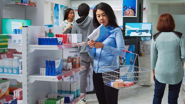 Cliente femminile che legge prescrizione su scatole di pillole, guardando farmaci e integratori sugli scaffali della farmacia. Donna che controlla i pacchetti di prodotti sanitari e prodotti farmaceutici.