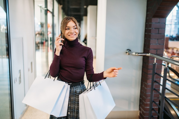 Foto cliente femminile con il sacchetto della spesa che comunica dal telefono nel centro commerciale.